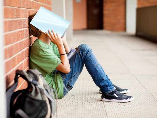 teen sitting at wall with a book over face