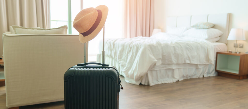 Black Luggage with hat in modern hotel room after door opening. Baggage for Time to travel, service, journey, trip, summer holiday and vacation concepts